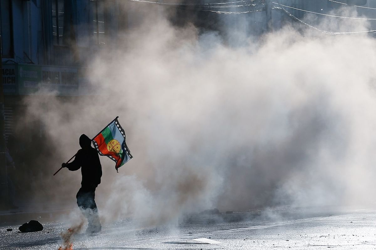A demonstrator with a Mapuche flag is seen through the tear gas during a rally against Chile's government on the second anniversary of the protests and riots that rocked the country. Credit: Reuters Photo
