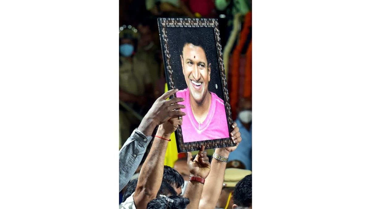 A fan holds a poster of Kannada film actor Puneeth Rajkumar as he arrives to pay his last respects to the mortal remains of Rajkumar. Credit: PTI Photo