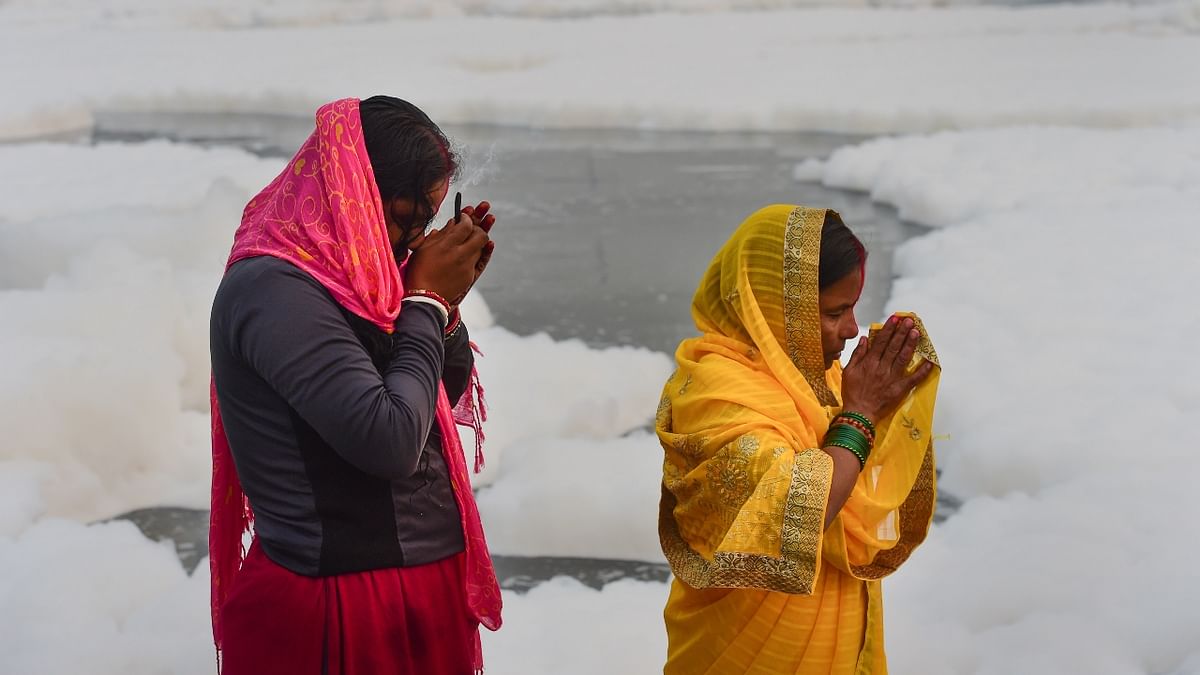 Devotees offer prayers to the rising sun as toxic foam floats on the surface of polluted Yamuna river during Chhath Puja celebrations in Yamuna, Delhi. Credit: PTI Photo