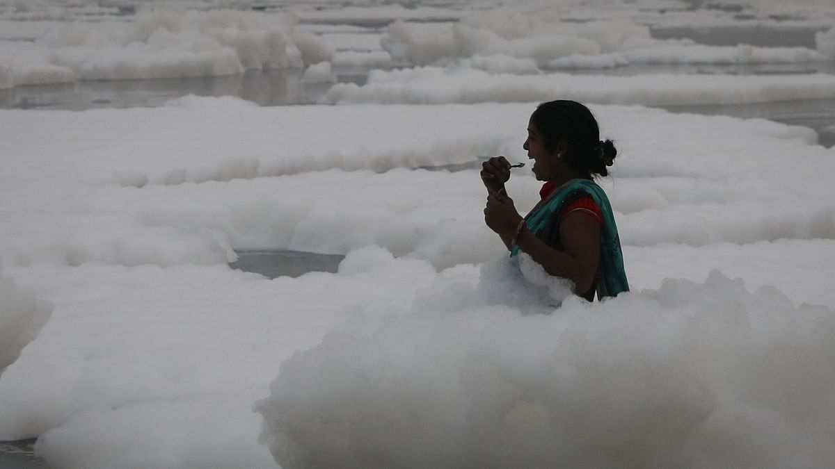 A woman brushes her teeth as she stands in knee-deep toxic foam in Yamuna river, Delhi. Credit: Reuters Photo