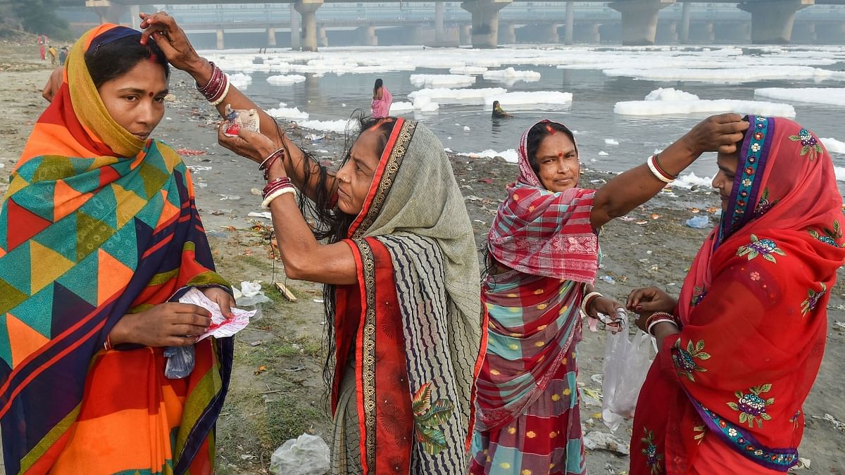 Women apply vermilion on each other's head after taking bath as part of the ritual of four days long Chhath Puja celebration, as toxic form floats on the surface of polluted Yamuna river at Kalindi Kunj, in New Delhi. Credit: PTI Photo