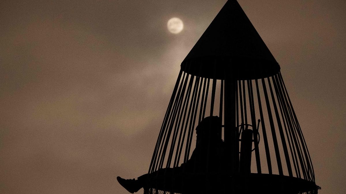 The moon shines though clouds as people sit inside a rocket ship-themed playground tower before a lunar eclipse in Torrance, California. Credit: AFP Photo