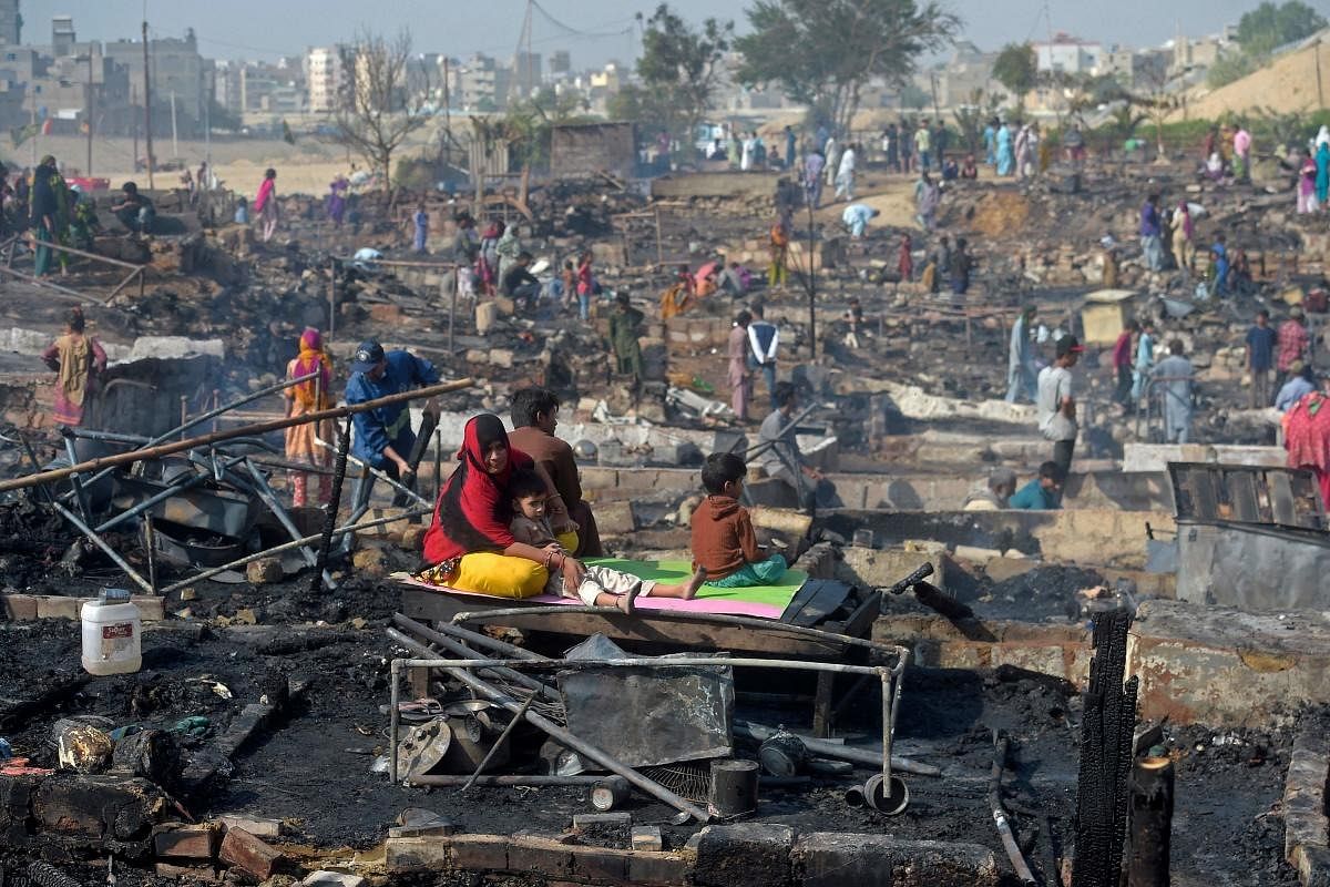 Residents sit amid debris of their burnt houses after a fire broke out in a slum area in Karachi. Credit: AFP Photo