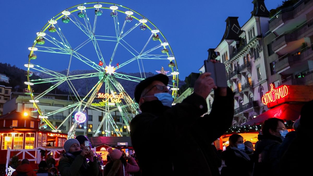 A person wearing a mask takes a picture of a sunset at the Christmas Market, amid the coronavirus disease (COVID-19) pandemic, in Montreux, Switzerland. Credit: Reuters Photo