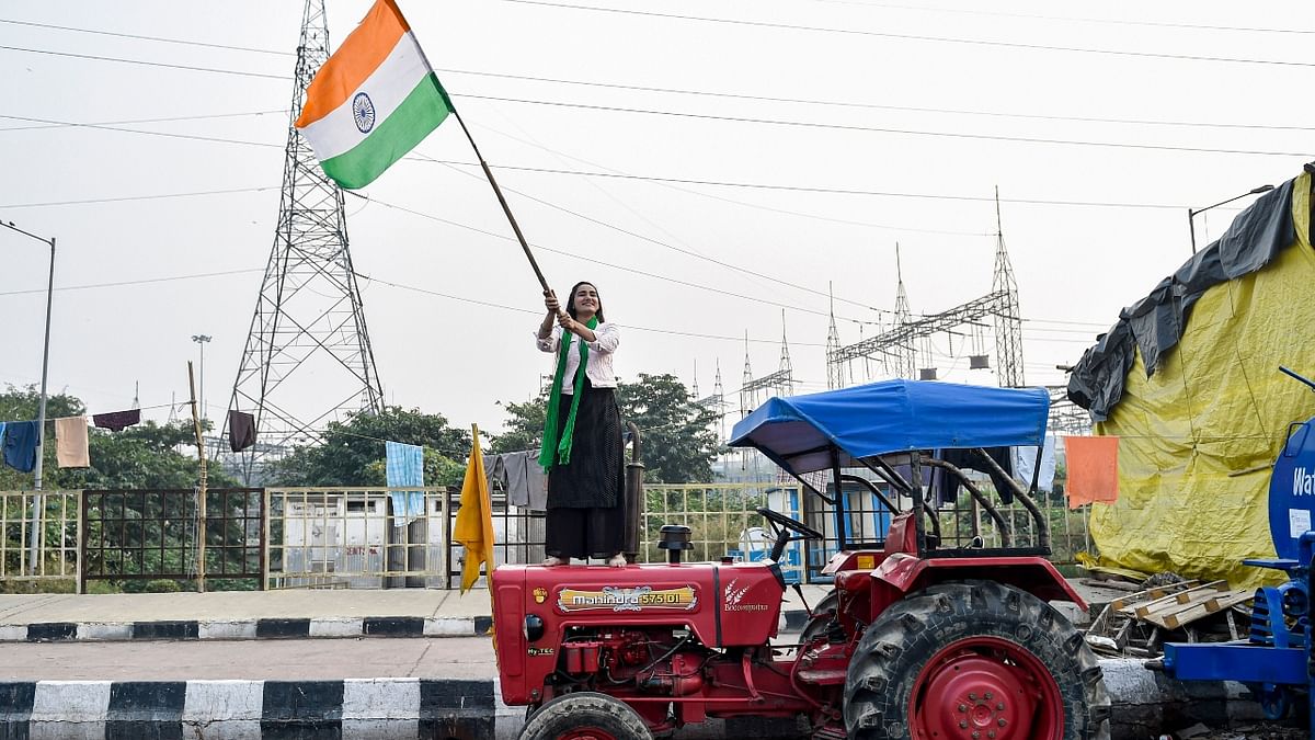 A protestor standing atop a tractor waves the national flag as she celebrates after a decision to withdraw farmers movement in the wake of the government accepting all demands put forward by the agitating farmers, at Ghazipur border in New Delhi. Credit: PTI Photo