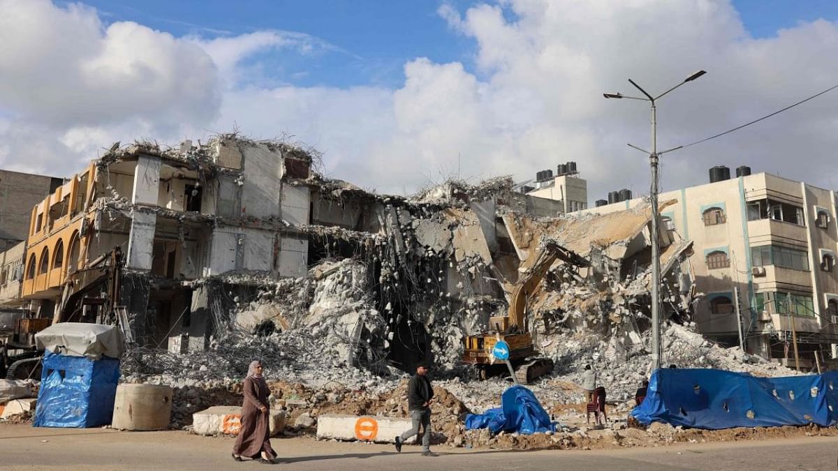 Palestinians walk past the al-Jawhara Tower in Gaza City's al-Rimal neighbourhood, which was targeted by Israeli airstrikes last May, as a bulldozer clears the rubble. Credit: AFP Photo
