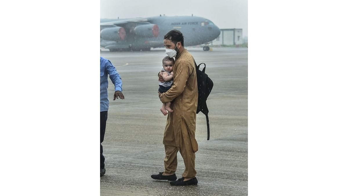 A man carries a child as people who were stranded in crisis-hit Afghanistan arrive by a special repatriation flight of IAF at the Hindan Air Force Station, in Ghaziabad. India airlifted nearly 400 people in three flights from Kabul in an operation that covered Indian citizens as well as Afghan nationals, including Sikhs and Hindus. Taliban took over Afghanistan in August 2021 after the chaotic withdrawal of the United States-led foreign forces. Credit: PTI Photo/Arun Sharma
