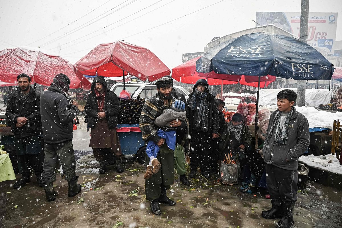 A man (C) holds a child as vendors wait for customers at a market during heavy snowfall in Kabul. Credit: AFP Photo