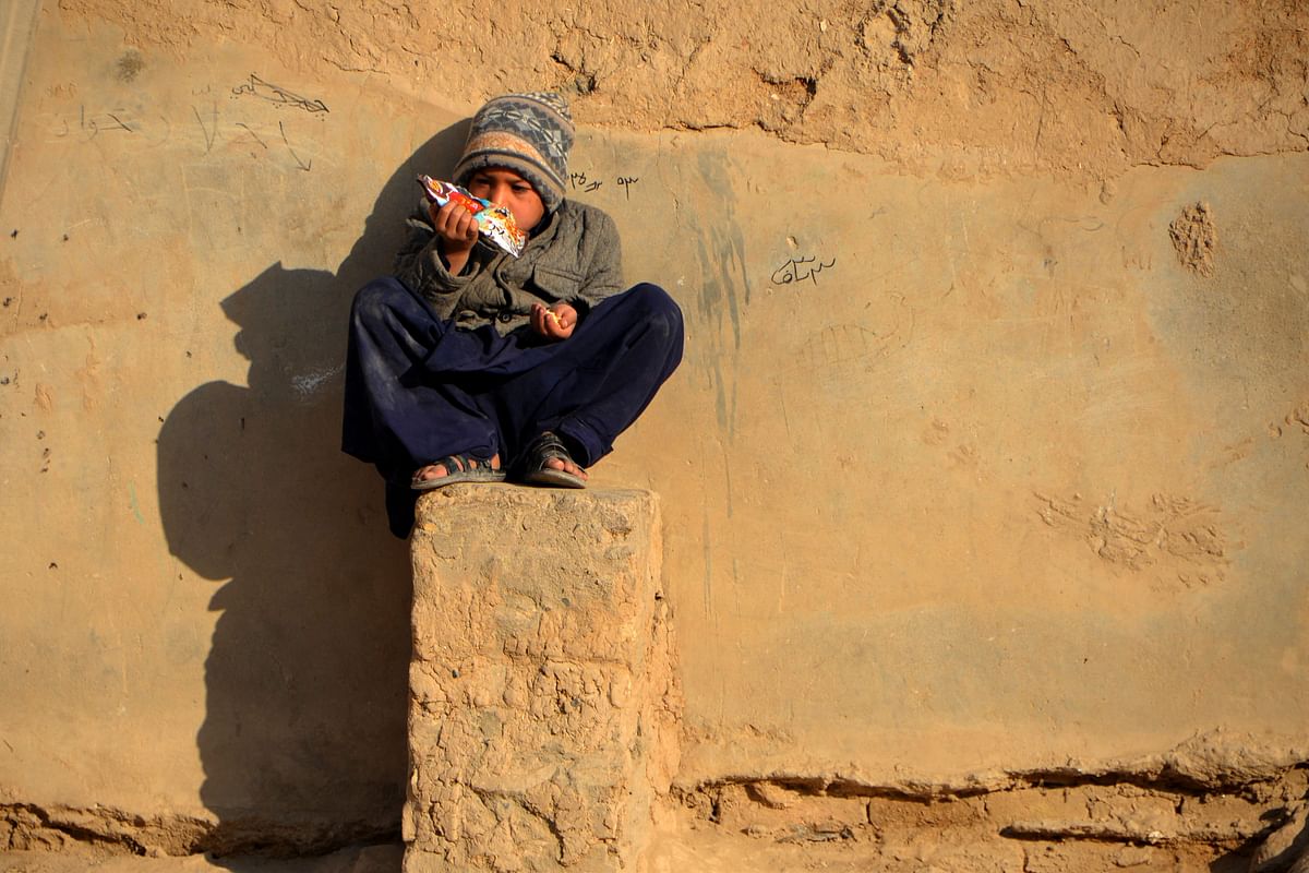An Afghan boy snacks while sitting on a plinth besides a mud house in Kandahar city. Credit: AFP Photo