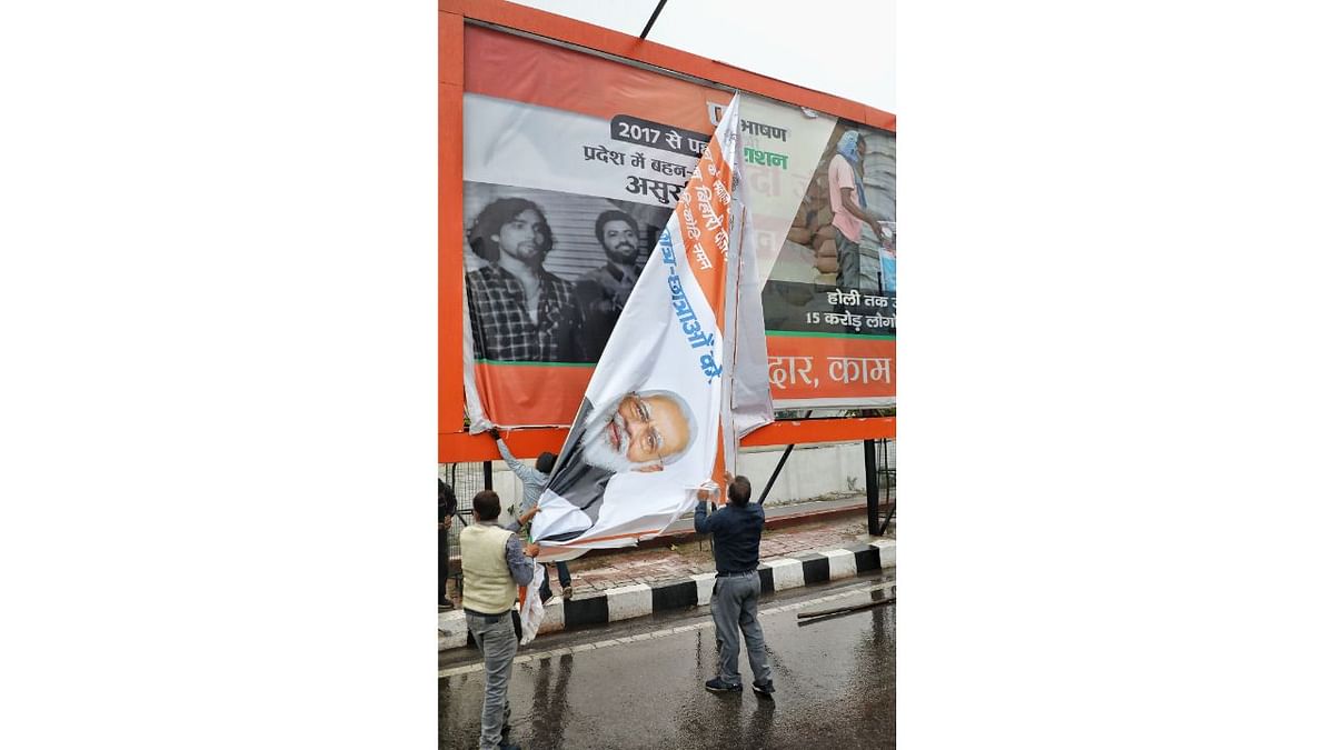 UP administration workers remove a political banner featuring Prime Minister Narendra Modi as the Model Code of Conduct has come into effect in UP. Credit: PTI Photo