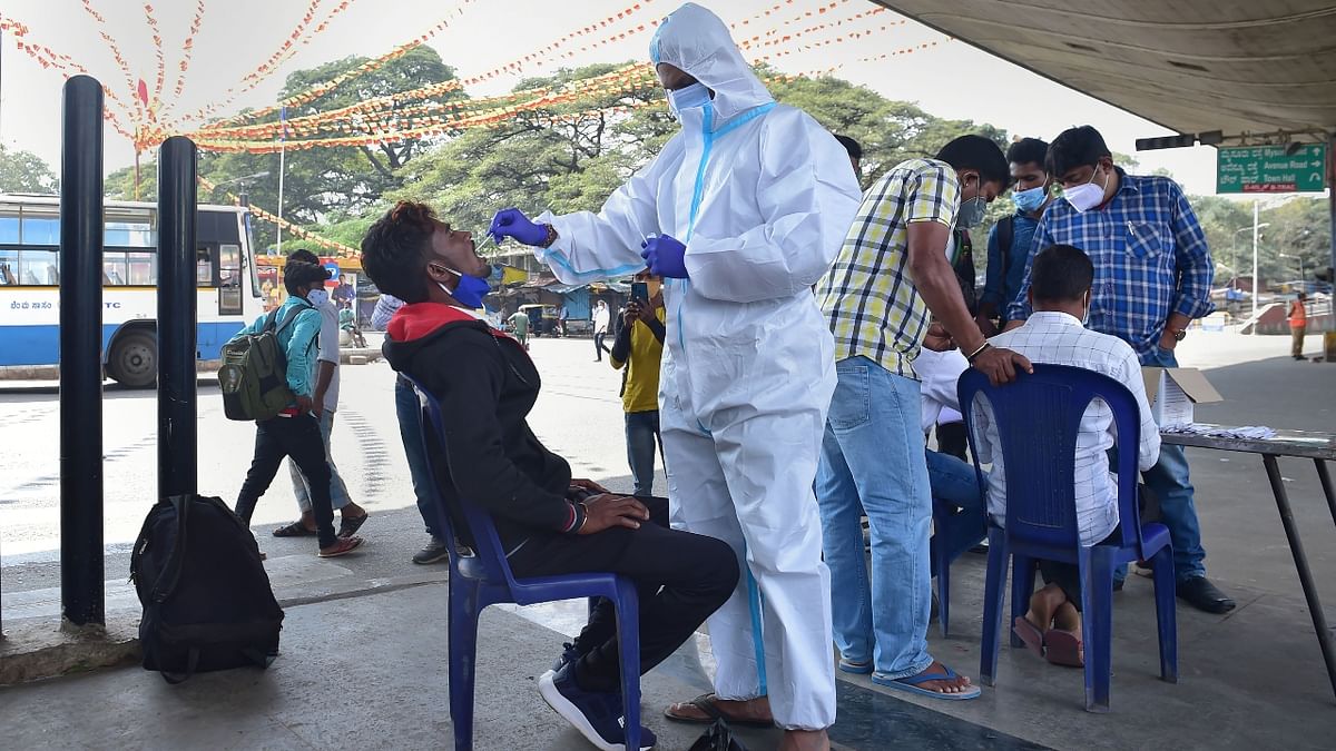 A health worker collects swab sample of a passenger for Covid-19 test at K R Market during the weekend curfew imposed by the Karnataka government to curb the spread of Covid-19, in Bengaluru. Credit: PTI Photo