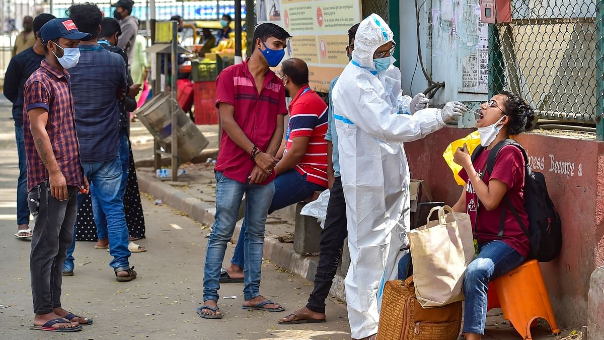 A health worker collects swab samples of passengers for Covid-19 test at KSR Railway Station during the 55-hour long weekend curfew in Bengaluru. Credit: PTI Photo