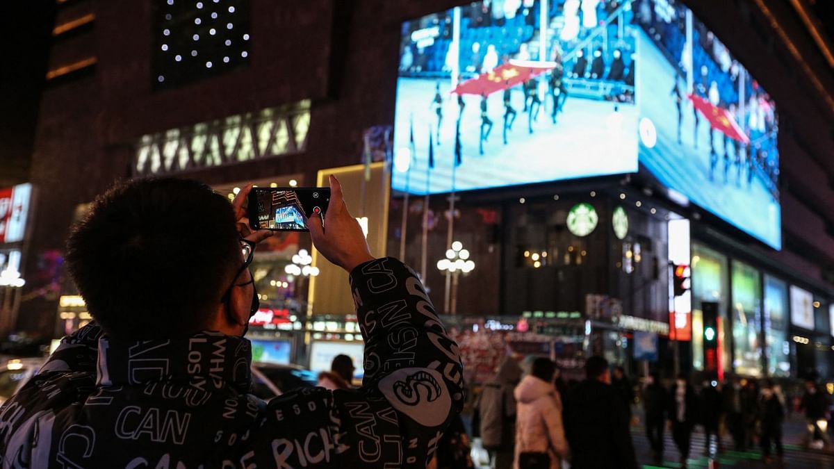 A man taking photos on a screen showing live footage of the opening ceremony of the Beijing 2022 Winter Olympic Games in Shenyang, in China's northeastern Liaoning Province. Credit: AFP Photo
