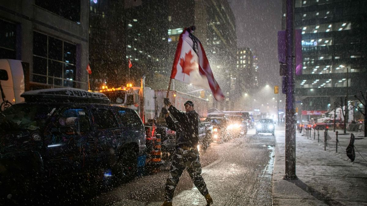 Snow falls around a demonstrator waving a flag during a protest by truck drivers over pandemic health rules and the Trudeau government, outside the parliament of Canada in Ottawa. Credit: AFP Photo
