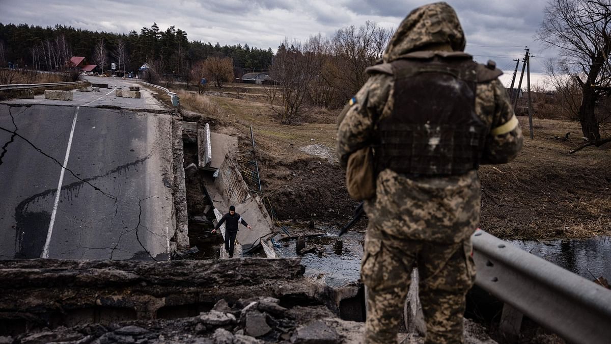 An Ukrainian serviceman looks at a civilian crossing a blown up bridge. Credit: AFP Photo
