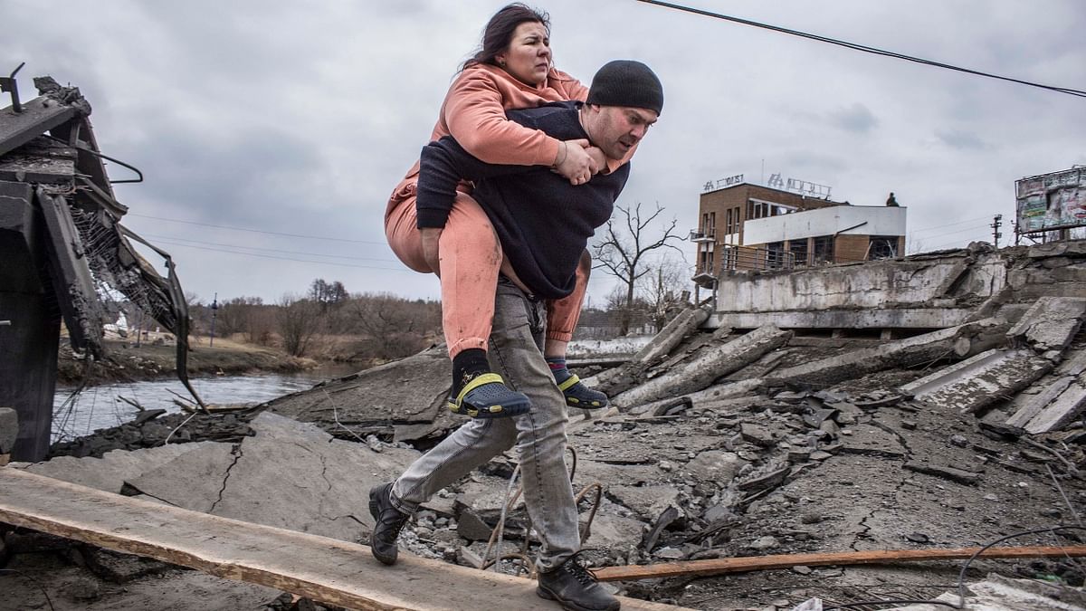 A man carries a woman as they cross an improvised path while fleeing the town of Irpin, Ukraine. Credit: AP Photo