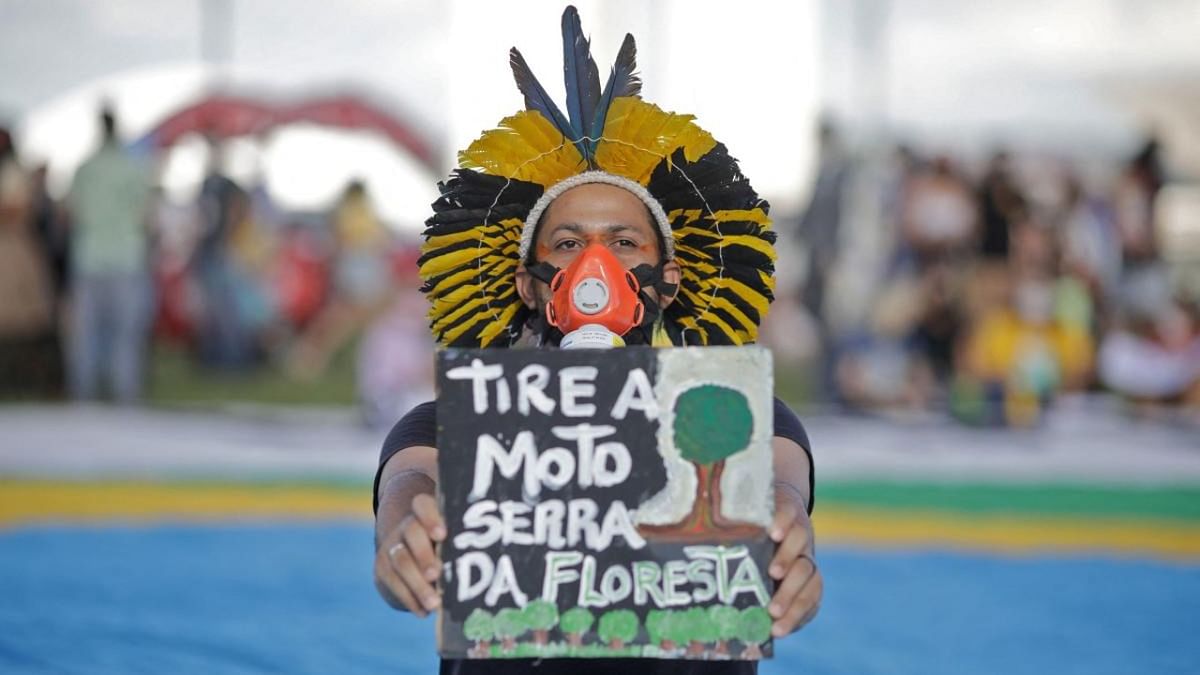 An indigenous man holds a sign reading “get the chainsaw out of the forest” during a demo led by Brazilian musician Caetano Veloso (out of frame) in defense of Earth and the environment and against the environmental policies of Brazilian President Jair Bolsonaro, outside the Congress building in Brasilia. Credit: AFP Photo