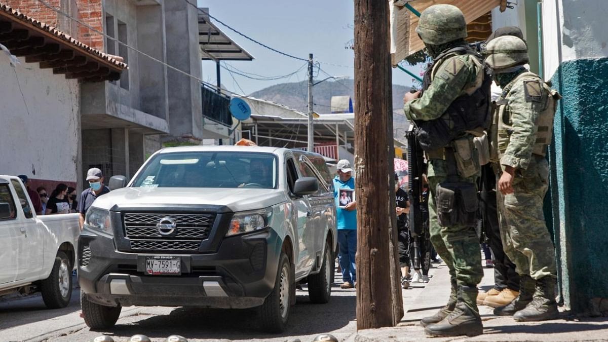 Soldiers stand guard as people accompany the car carrying the coffin with the remains of Mayor Cesar Arturo Valencia, during his funeral in Aguililla, Michoacan state, Mexico. Credit: AFP Photo