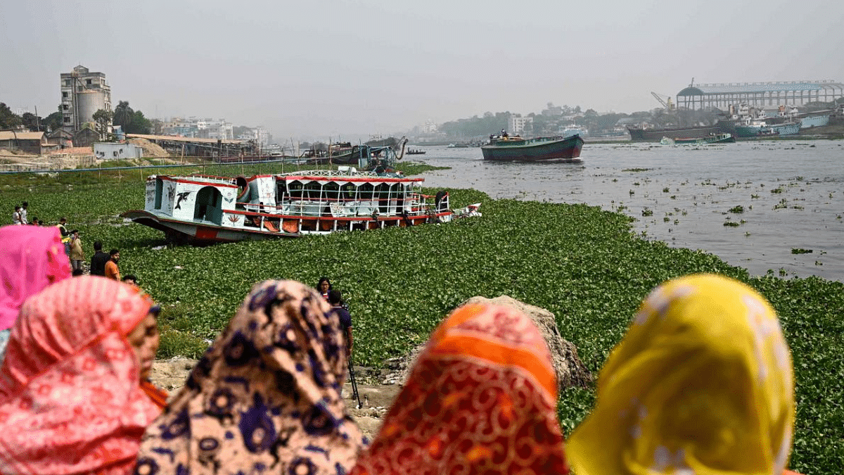 People watch the rescued ferry following an accident in the Shitalakshya River in Narayanganj on March 21, 2022. - At least six people are dead and dozens more are believed missing after a bulk carrier crashed into a small ferry in a river near Bangladesh's capital. Credit: AFP Photo