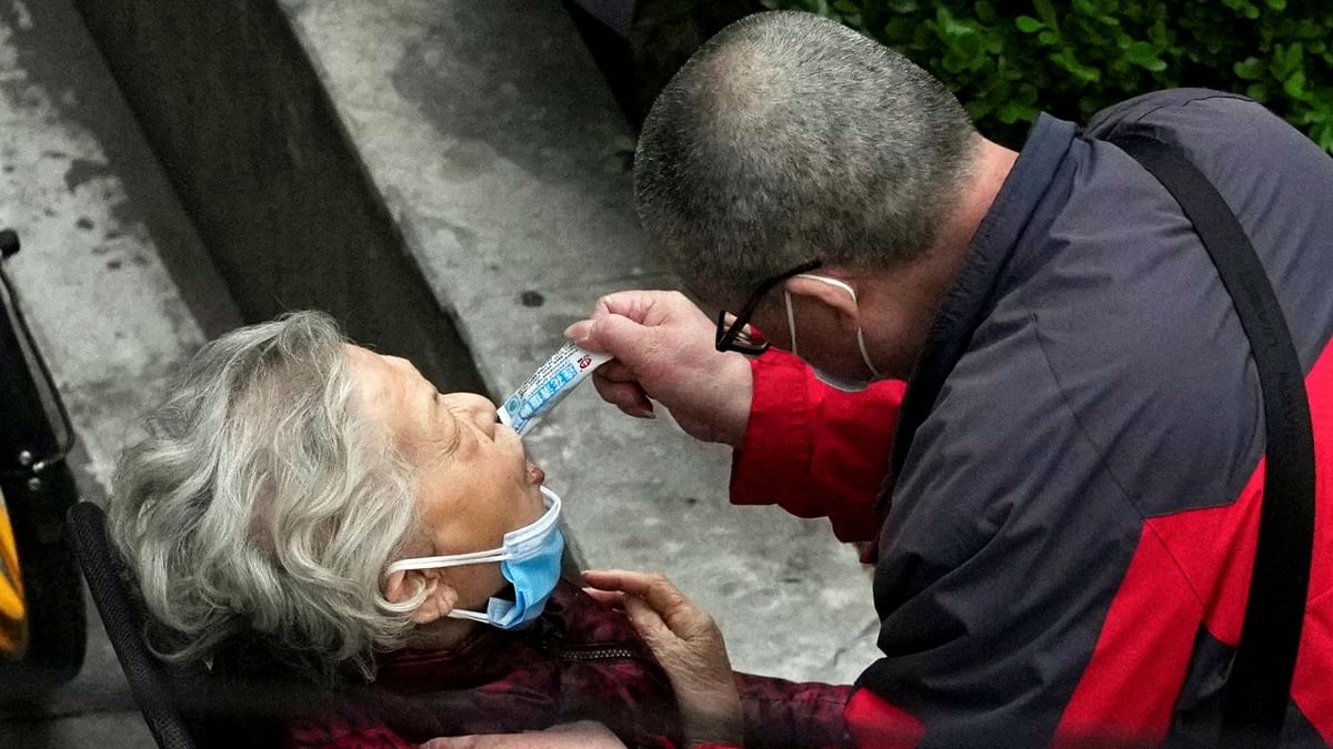 A man helps a woman consume a packet of traditional Chinese medicine, as she sits by the side of a road outside a residential compound, during a lockdown to curb the spread of the coronavirus disease in Shanghai. Credit: Reuters Photo