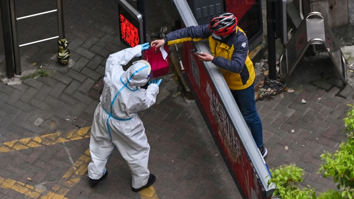 A worker wearing protective gear receives essentials from a delivery worker at the entrance of a compound during the second stage of a pandemic lockdown in Jing'an district in Shanghai. Credit: AFP Photo