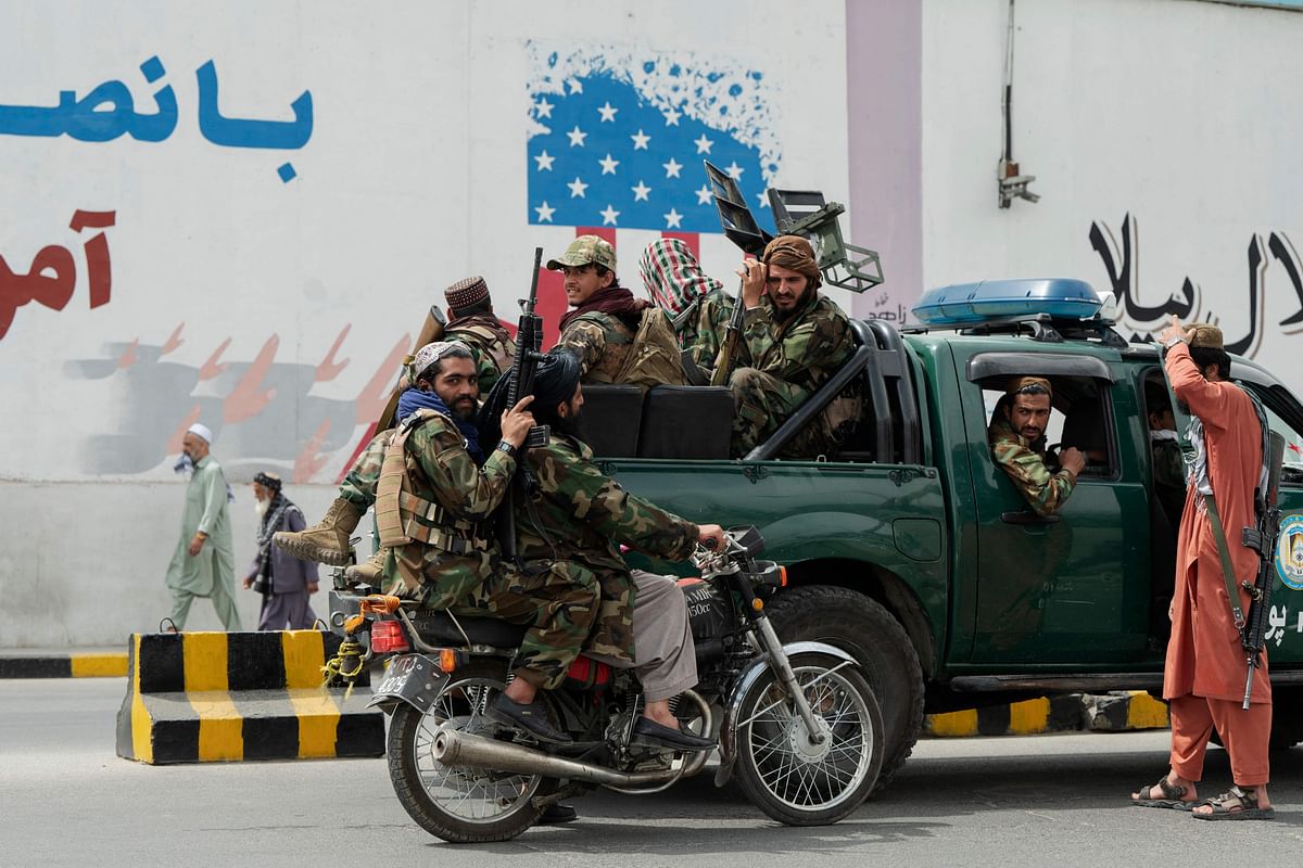 Taliban fighters on the back of a vehicle and on a motorbike gather in front of a mural wall outside the US embassy in Kabul. Credit: AFP Photo