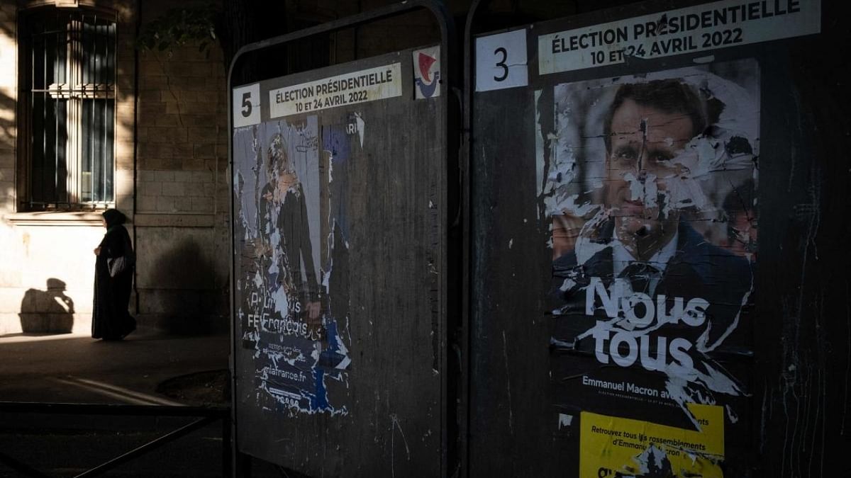 This photograph taken on April 21, 2022 in Paris shows a veiled woman walking past campaign posters of French President Emmanuel Macron (R) and far-right presidential candidate Marine Le Pen. Credit: AFP Photo