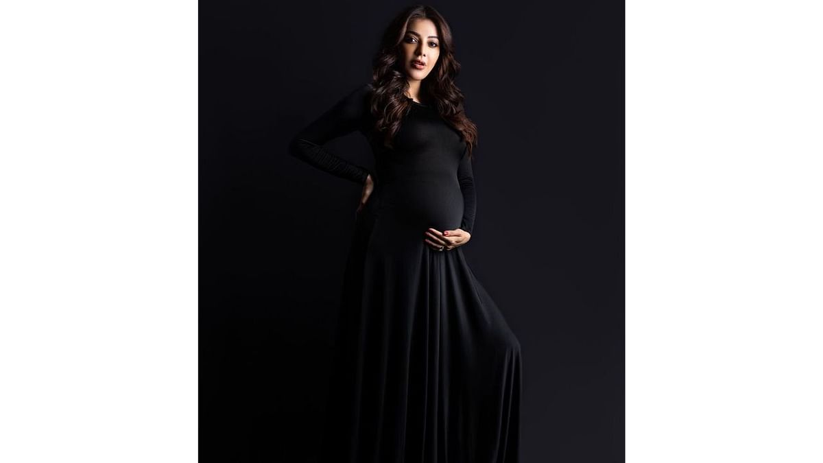 Kajal cradles her baby bump as she poses in a black pleated dress for a photoshoot. Credit: Instagram/kajalaggarwalofficial