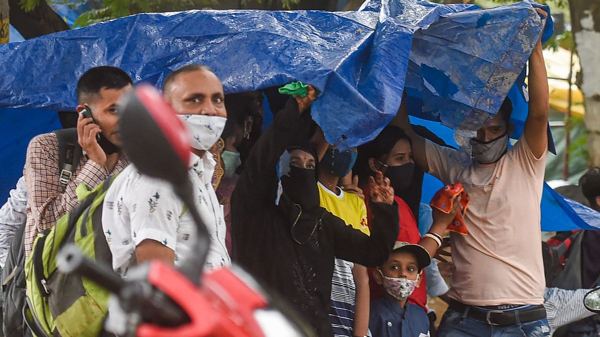 People shield themselves with a tarp following the rains in New Delhi. Credit: PTI Photo