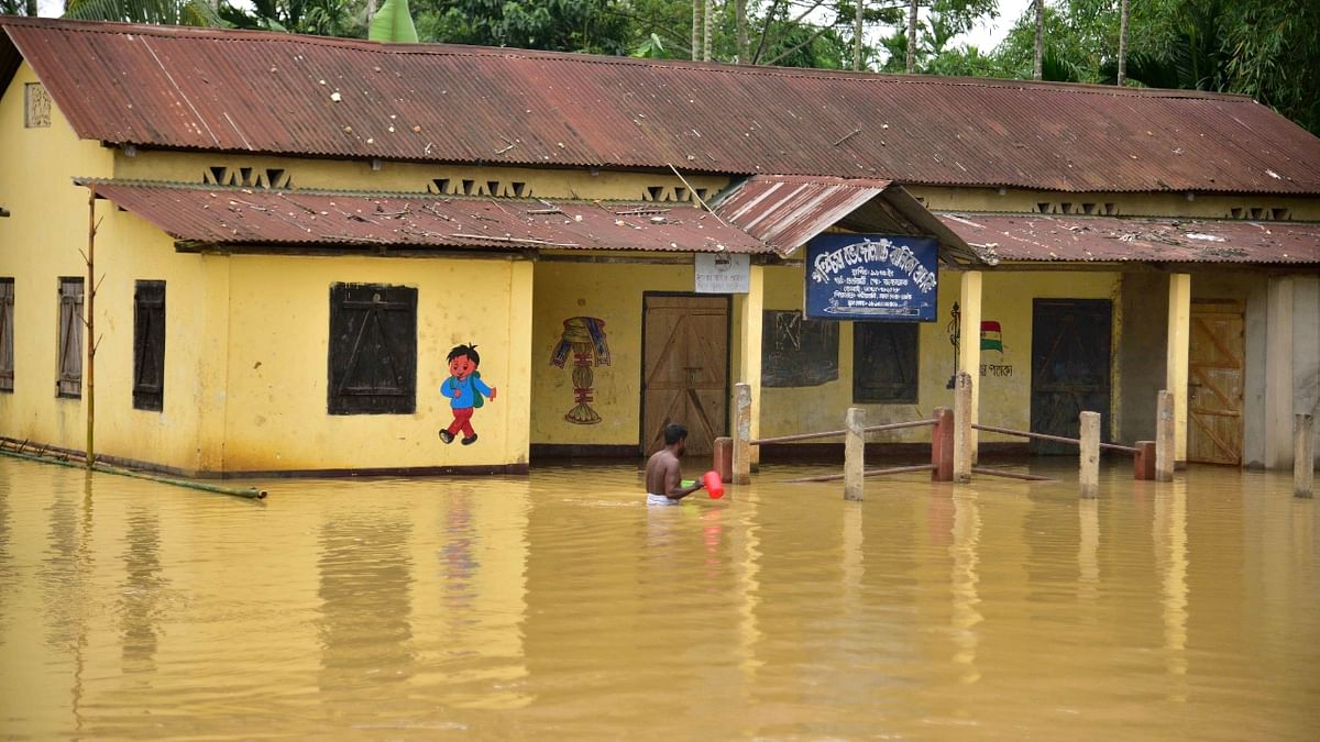 A man wades past a partially submerged school in a flood-affected area, following heavy rains in Hojai district of Assam. Credit: PTI Photo