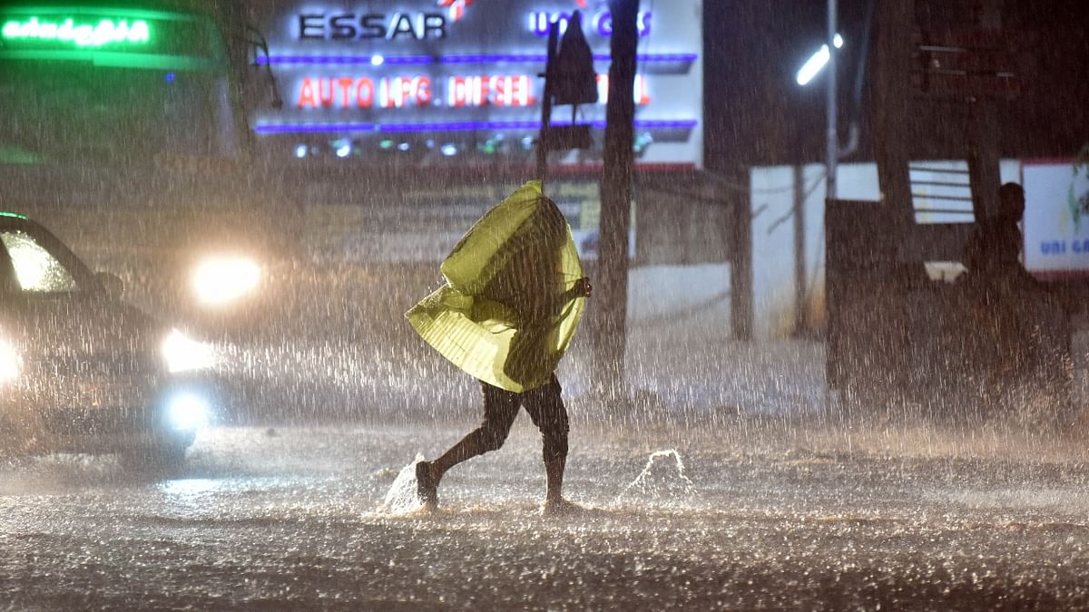 A man walks along a waterlogged street during heavy rain in Bengaluru. Credit: DH Photo/Anup Ragh T