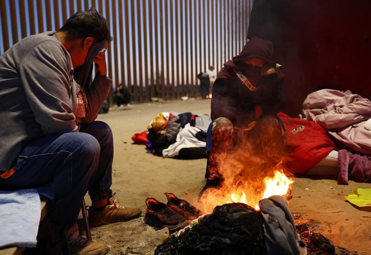 Immigrants warm themselves by a fire before sunrise along the U.S.-Mexico border barrier as they await processing by the US Border Patrol after crossing from Mexico. Credit: AFP Photo