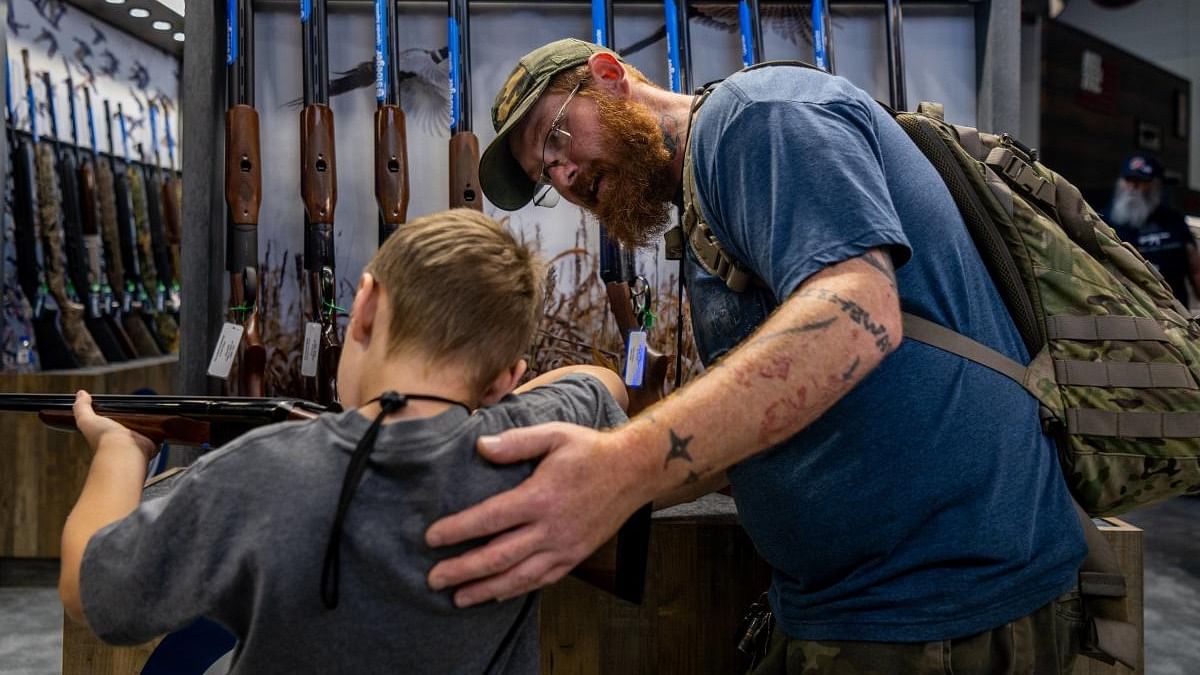 Chris Shelton, 36, helps his son Luke Shelton, 7, steady a firearm at the George R. Brown Convention Center during the National Rifle Association (NRA) annual convention on May 28, 2022 in Houston, Texas. Credit: AFP Photo