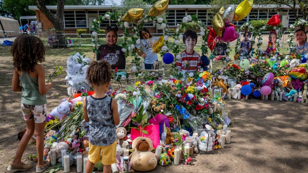 Siblings Thalia (L), and Thomas Huff pay their respects at a memorial dedicated to the 19 children and two adults killed on May 24th during the mass shooting at Robb Elementary School on May 31, 2022 in Uvalde. Credit: AFP Photo
