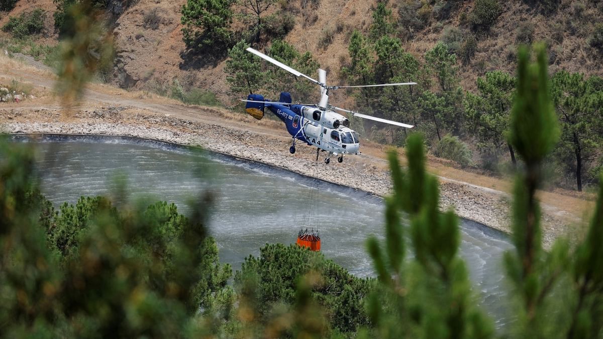 A helicopter fills a bucket with water to make a water drop over a wildfire near the houses in Benahavis, Spain. Credit: Reuters Photo