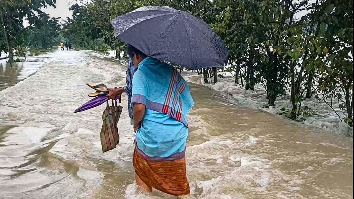 Villagers wade through a flooded street after heavy rainfall, at Sarukhetri village in Barpeta district, Assam. Credit: PTI Photo