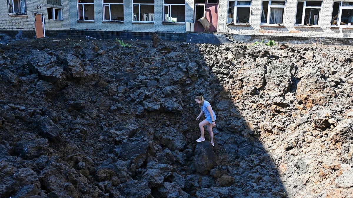 A woman stands in a crater caused by missile strikes which struck the yard of a school in a residential area of Kharkiv. Credit: AFP Photo