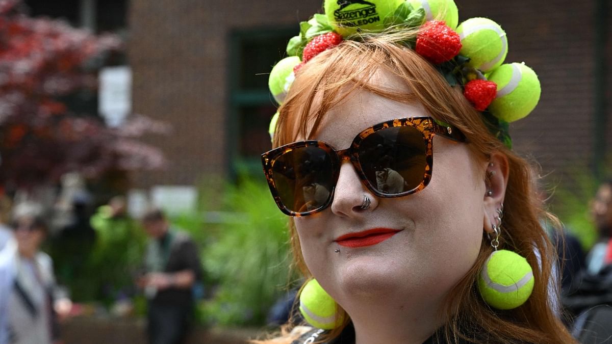 A woman sporting a strawberry and tennis ball hair ornament poses at The All England Tennis Club in Wimbledon, southwest London on the third day of the 2022 Wimbledon Championships. Credit: AFP Photo