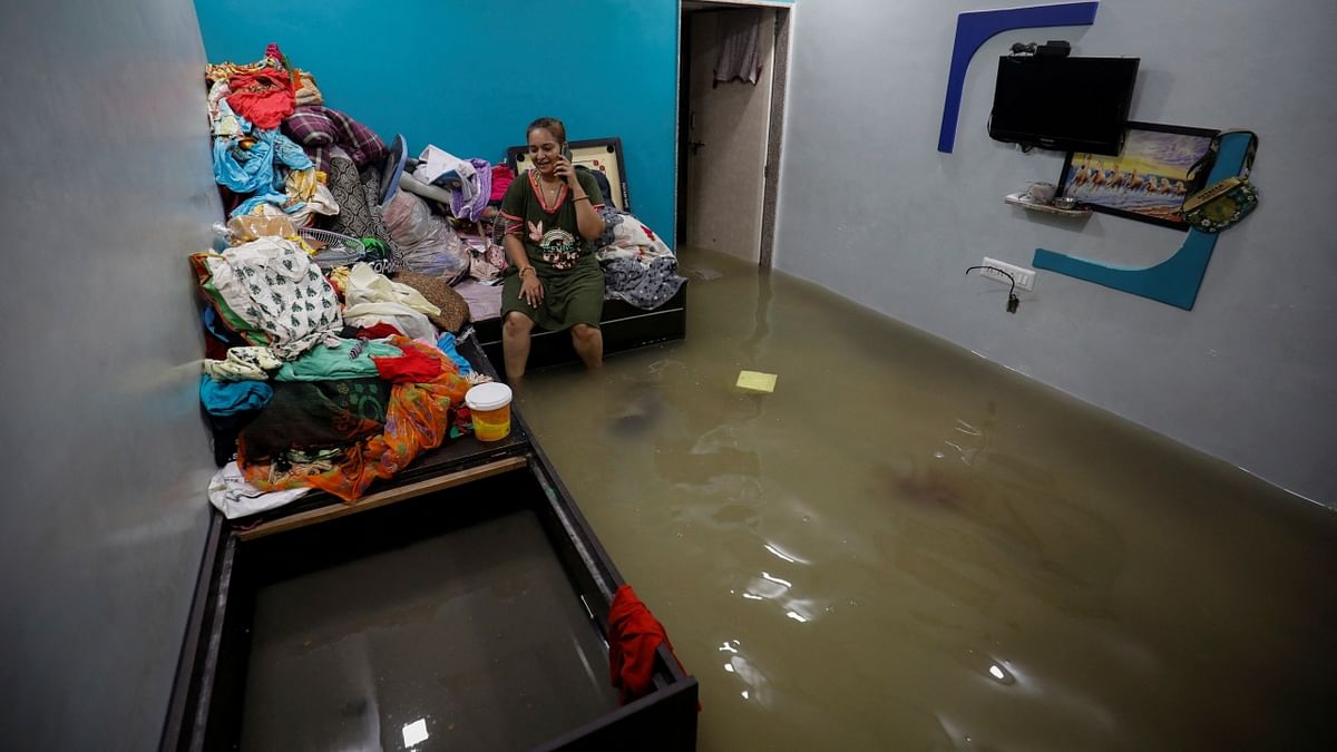 A woman talks on a mobile phone as she sits on a bed inside her flooded room after heavy rains in Ahmedabad. Credit: Reuters Photo