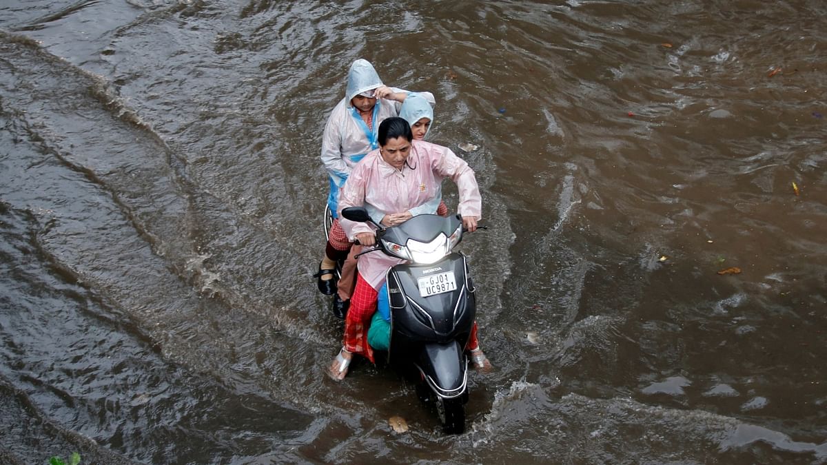 A woman with her children, balances her scooter as she moves through a water-logged road after heavy rains in Ahmedabad. Credit: Reuters Photo