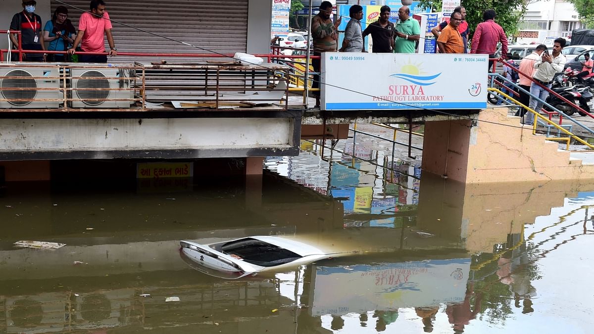 Ahmedabad: People look at a submerged car in a flooded commercial complex after heavy rains. Credit: AFP Photo