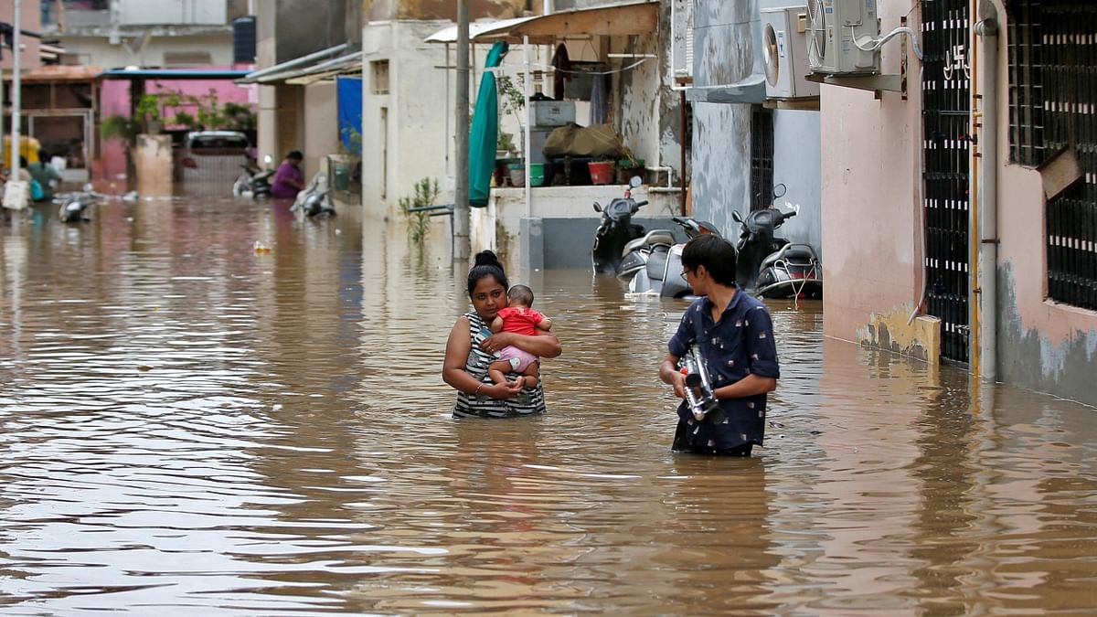 Ahmedabad: A woman carries her infant through a water-logged neighbourhood after her house was inundated with flood water following heavy rains. Credit: Reuters Photo