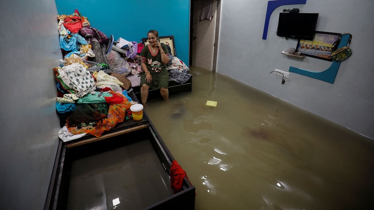 Ahmedabad: A woman talks on a mobile phone as she sits on a bed inside her flooded room after heavy rains. Credit: Reuters Photo