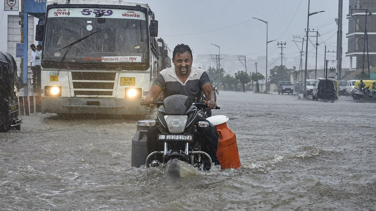 Rajkot: A man riding a motorcycle wades through the waterlogged Ring Road after monsoon rains. Credit: PTI Photo
