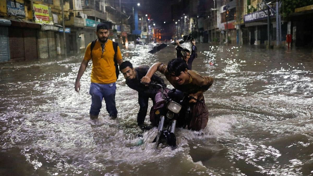 Boys push their motorcycle after it was stopped on a flooded street, following heavy rains during the monsoon season in Karachi. Credit: Reuters photo