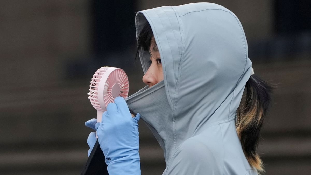 A woman uses a fan as she wears a cloth that protects her from the sun on a street, amid a heatwave warning in Shanghai, China. Credit: Reuters Photo