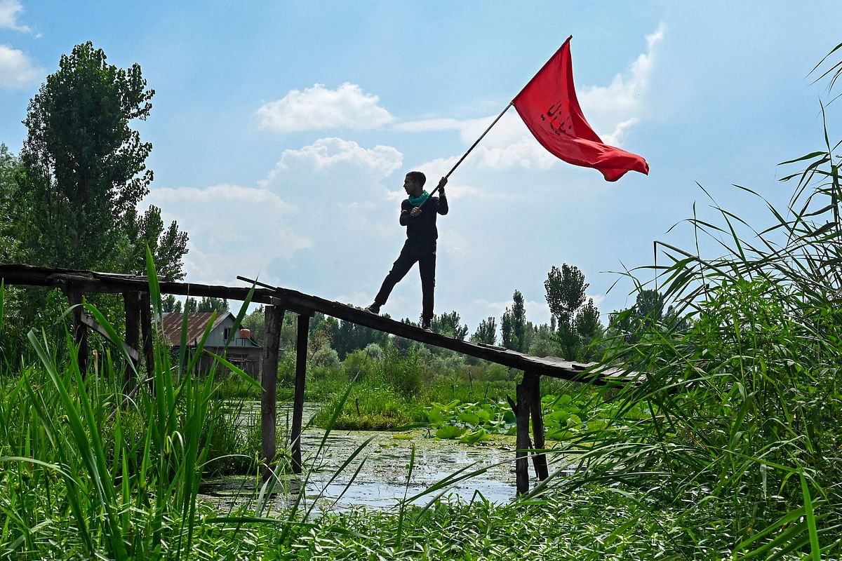 A Shiite Muslim mourner waves a religious flag during a Muharram procession on the ninth day of Ashura in the interiors of Dal Lake in Srinagar. Credit: AFP Photo