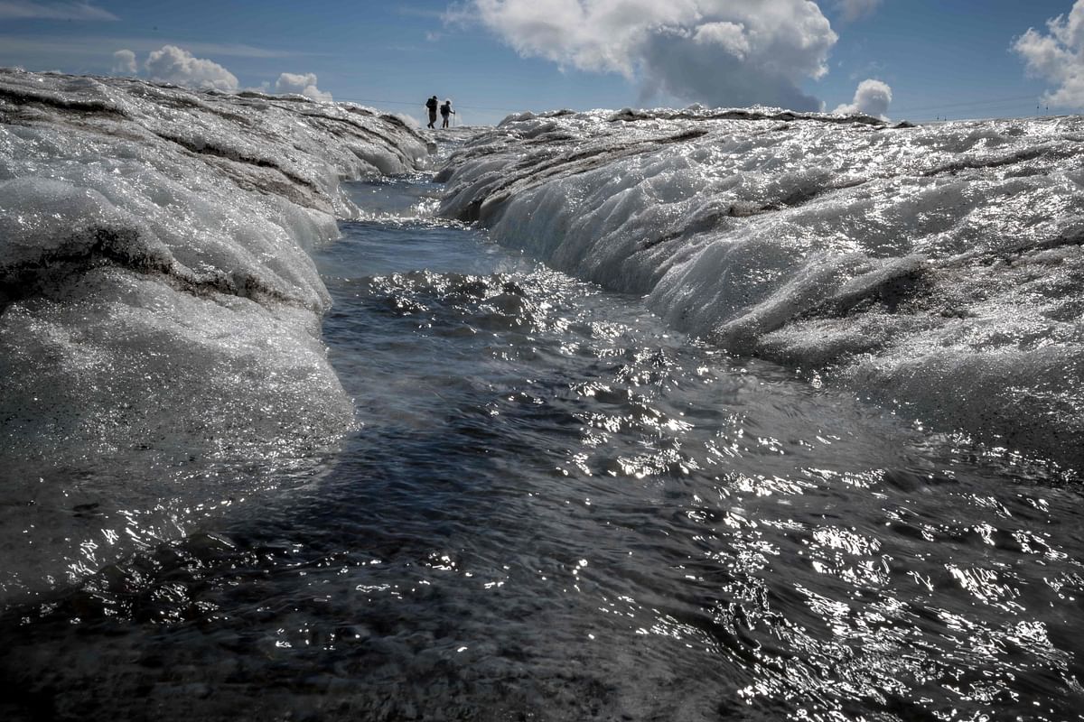 This picture taken on August 6, 2022 shows tourists walking next to a meltwater stream flowing from the Tsanfleuron Glacier above Les Diablerets, Switzerland. Credit: AFP Photo