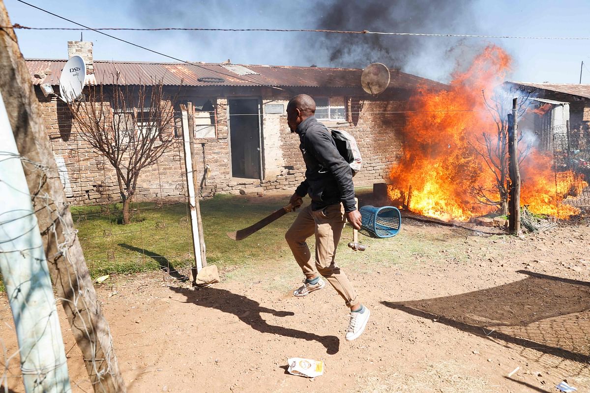 A Mohlakeng community member holds a machete and a hammer as residents run away from a fire set that is burning belongings of suspected illegal miners at a Mohlakeng Hostel, near Randfontein. Credit: AFP Photo