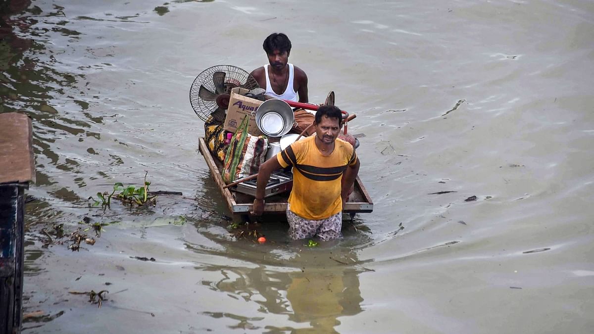 People wade through a waterlogged road to shift their belongings following incessant monsoon rains, at a flood-hit residential colony in Prayagraj. Credit: PTI Photo
